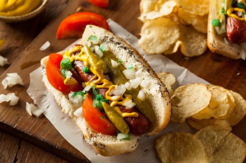 chicago style hot dog with neon relish, onions, tomato wedges, dill pickle spear, yellow mustard, sport peppers, celery salt and poppyseed bun